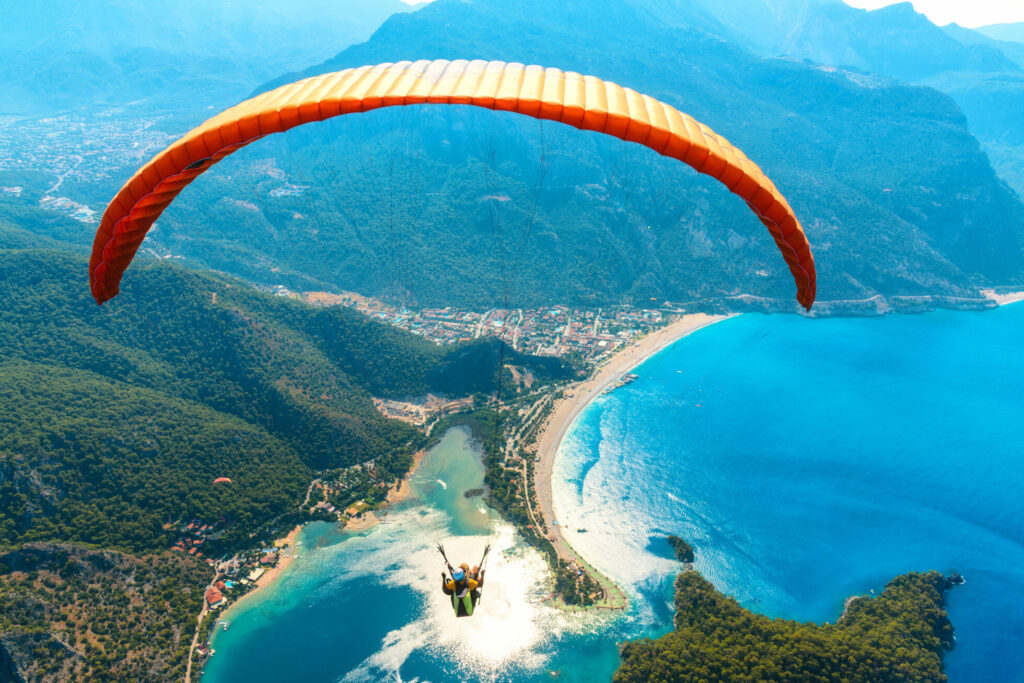 Paraglider tandem flying over the sea with blue water and mountains