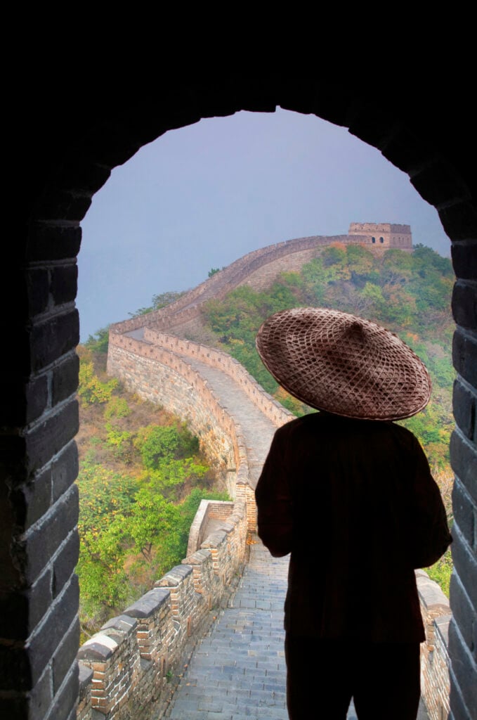 Man in arched doorway overlooking Great Wall of China.