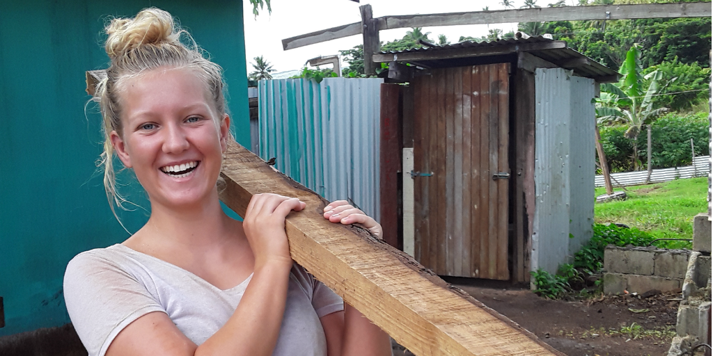 A volunteer carrying a wooden beam and smiling.