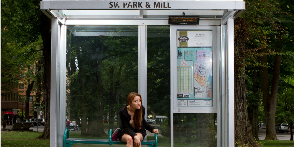 A woman waiting for a bus under a bus shelter.