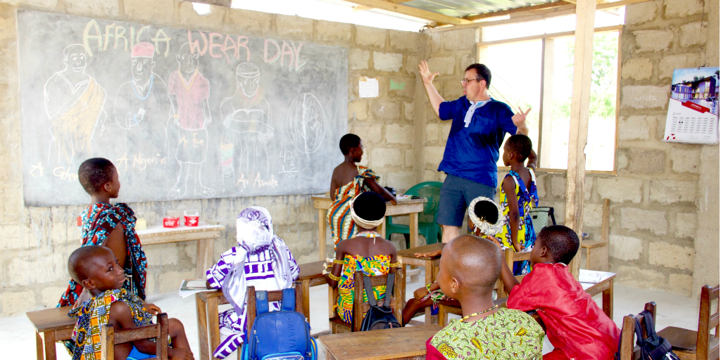 A volunteer in a classroom with Ghanaian children dressed in traditional Ghanaian dress.