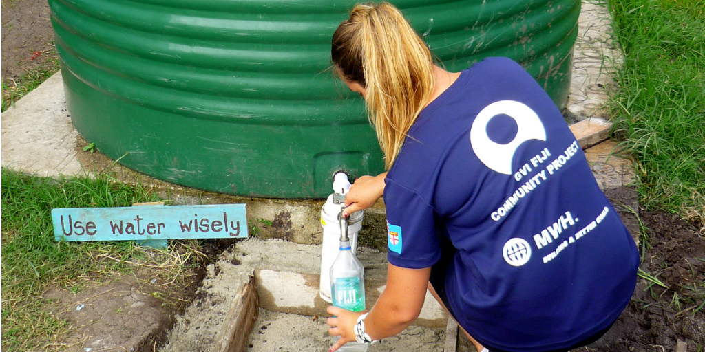 A volunteer filling a water bottle from a rain harvesting water tank.