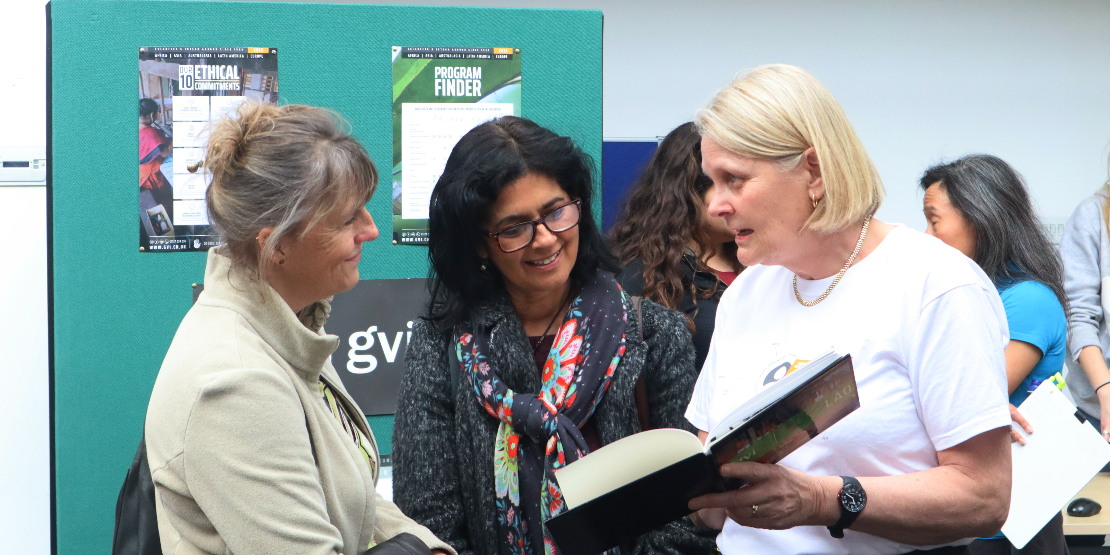 A GVI ex volunteer showing two interested women a page in a book.