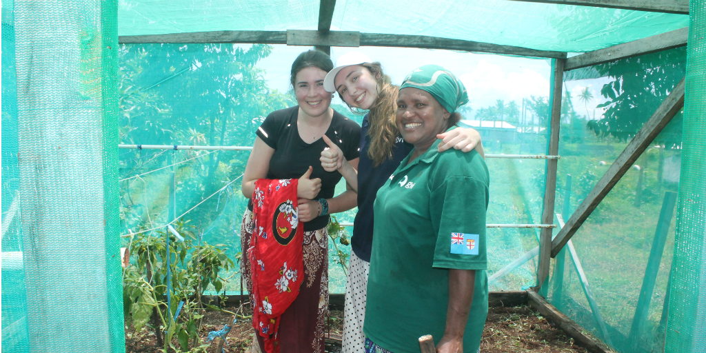 Volunteers with a local Fijian woman, standing in a greenhouse.