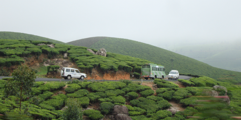 Vehicles driving along a dirt road on a green hillside.