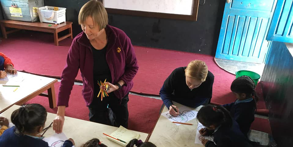 An adult volunteer distributes school supplied to learners in Nepal. As an older adult, you can really make an impact on top volunteer abroad programs.