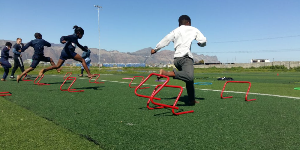 Children jump hurdles on a sports field in Cape Town, South Africa. Helping learners to be active and understand the benefits of a healthy lifestyle is one of the top reasons to volunteer.