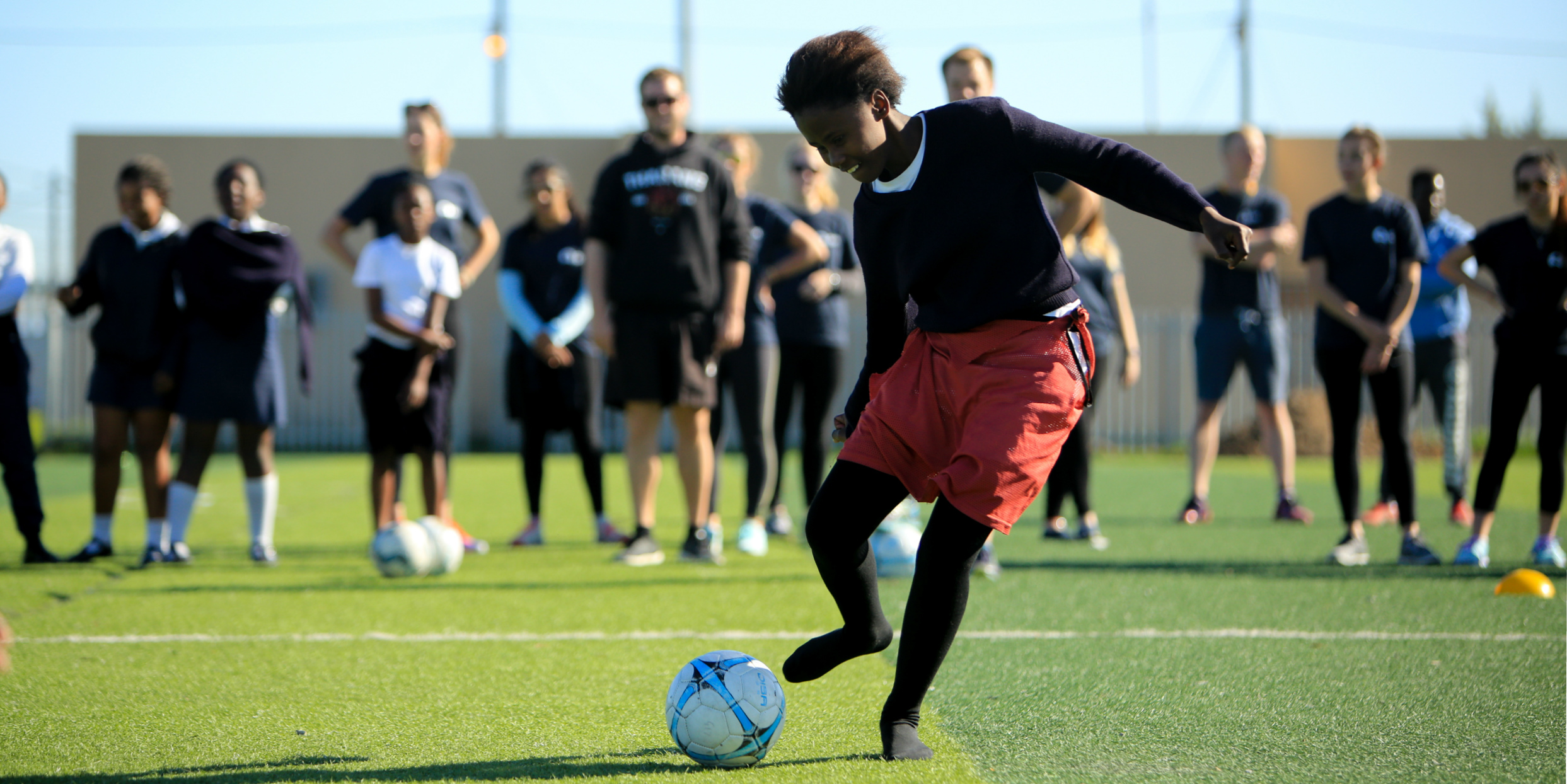A girl goes in to kick a soccer ball triumphantly. As part of activities for women's empowerment, GVI participants facilitate sports lessons with Cape Town youth.