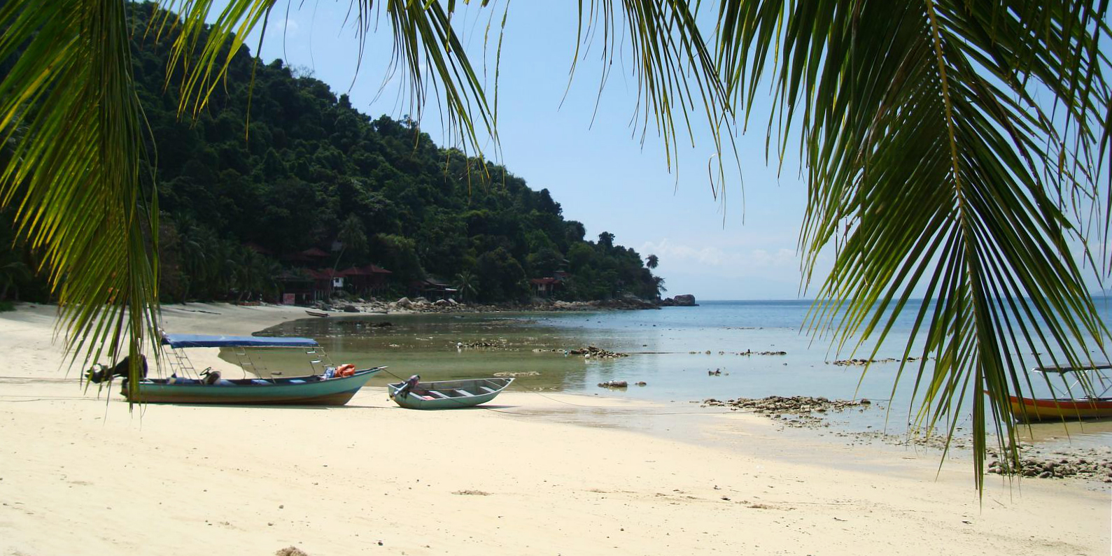 An idyllic scene of a wooden fishing boat on a Perhentian Island beach.