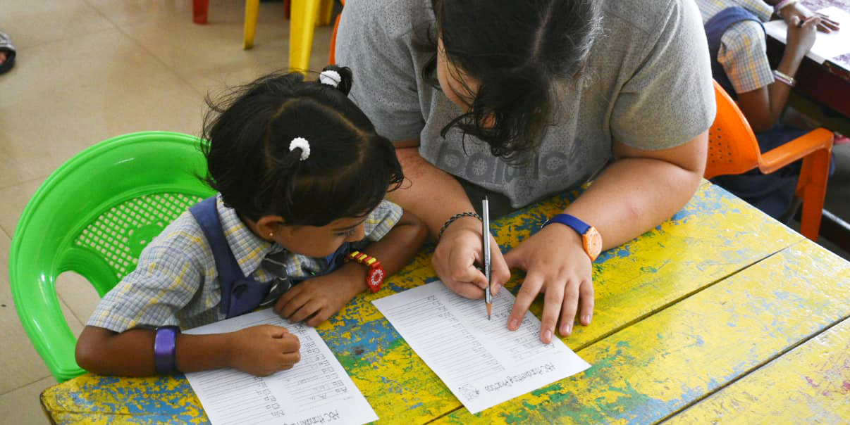 A GVI participant helps a learner complete a worksheet while volunteering in India.