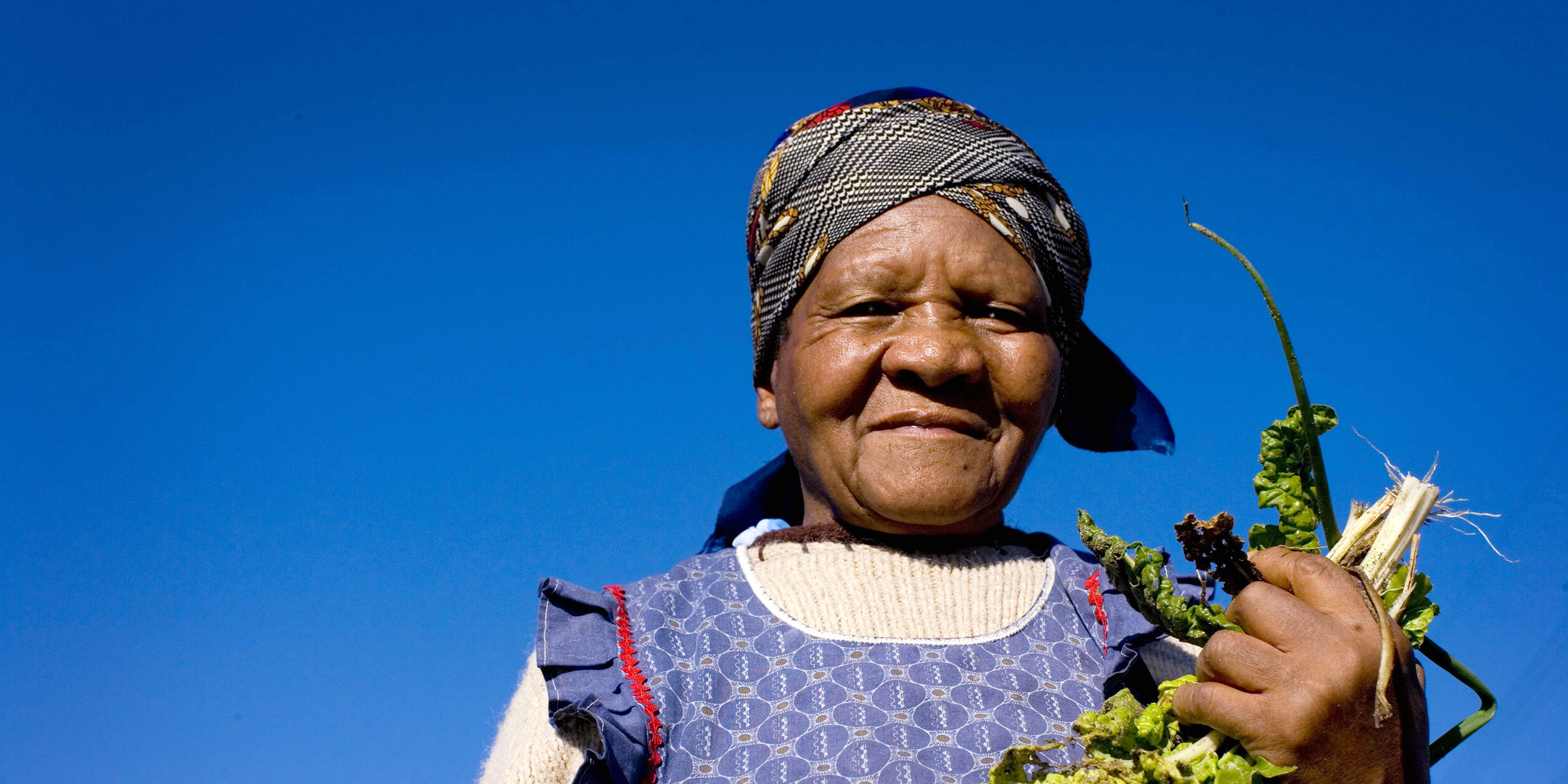 A woman poses with the fresh produce she has grown. Women's empowerment initiatives can focus on food growing schemes to keep communities healthy, and increase economic opportunities.