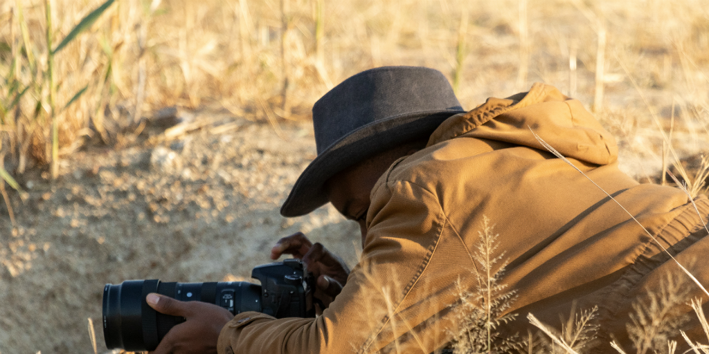 GVI volunteer lying on the ground to take a photo in the field