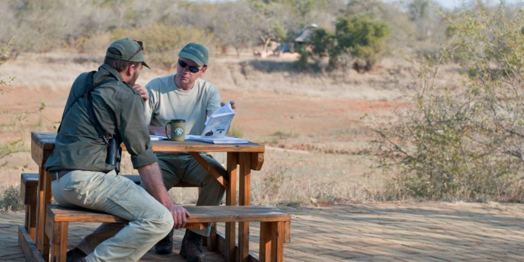 Two volunteers sitting together at a picnic table in a grassy plane