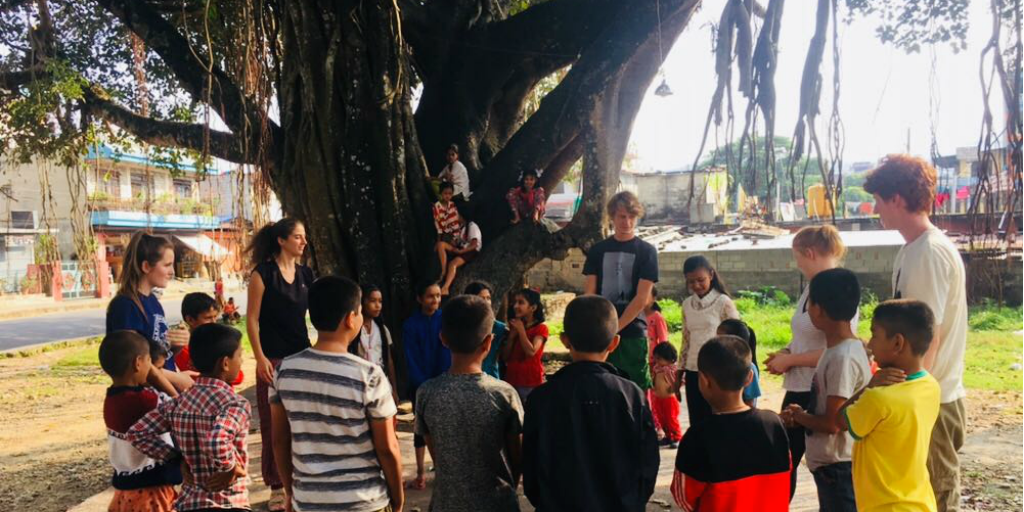 Childrn from Pokhara gather under a large tree with volunteers from GVI.