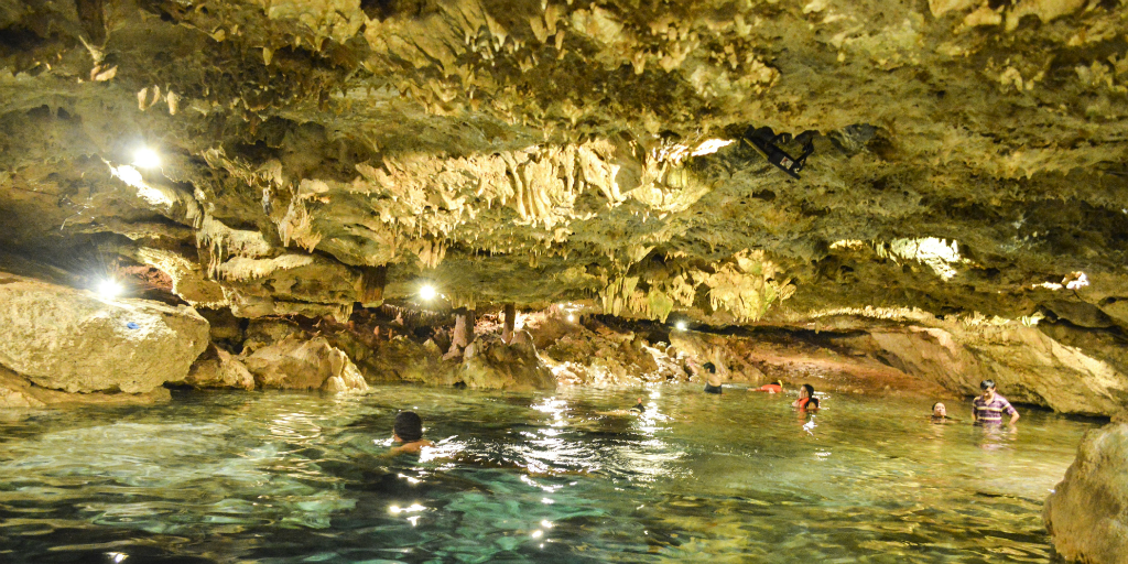People swimming in a cenote in Cancun with stalactites overhead.