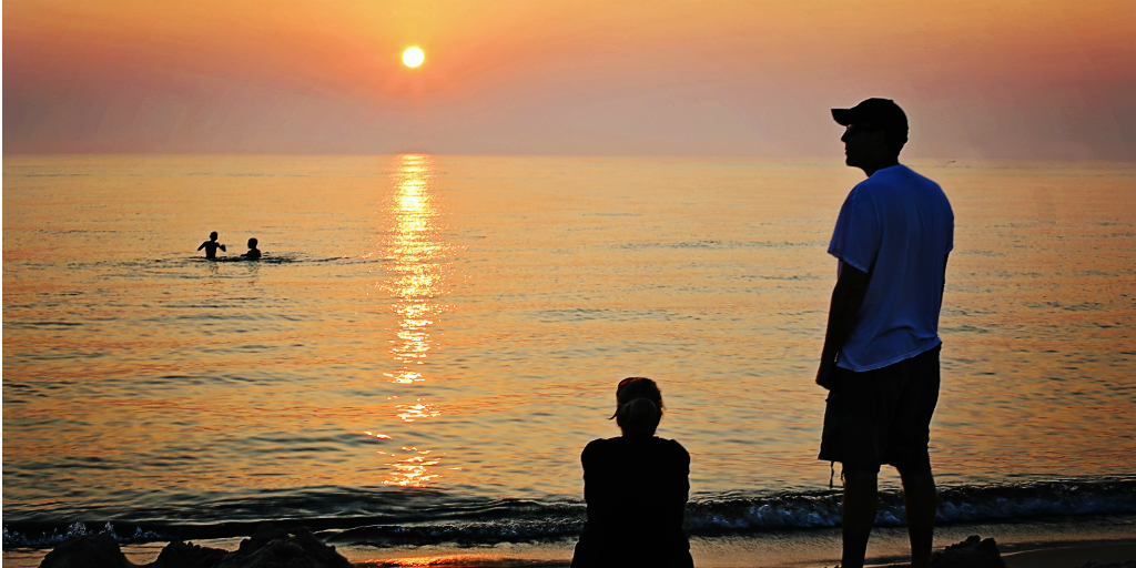 Children swimming at a beach with their parents looking on from the shore