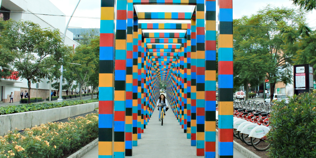 A girl riding her bike down a pathway under an art deco archway in Peurto Morelos, Mexico.