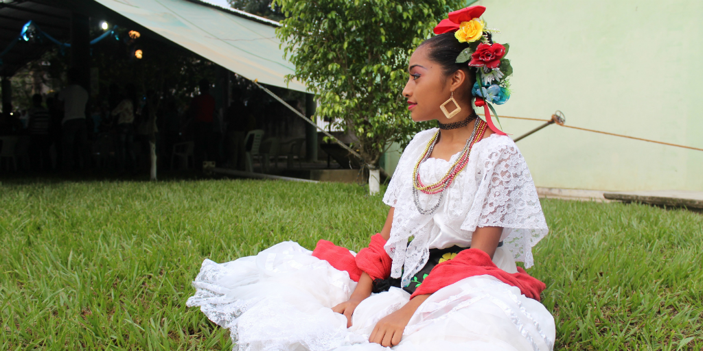 A Mexican woman in traditional dress sitting on grass.