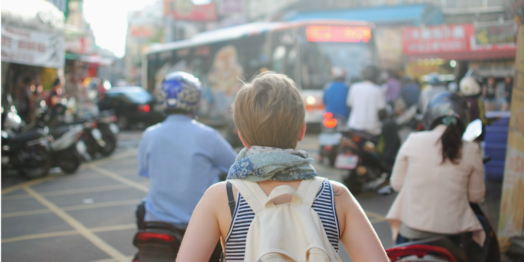A woman wearing a back pack, walking into a crowded street.