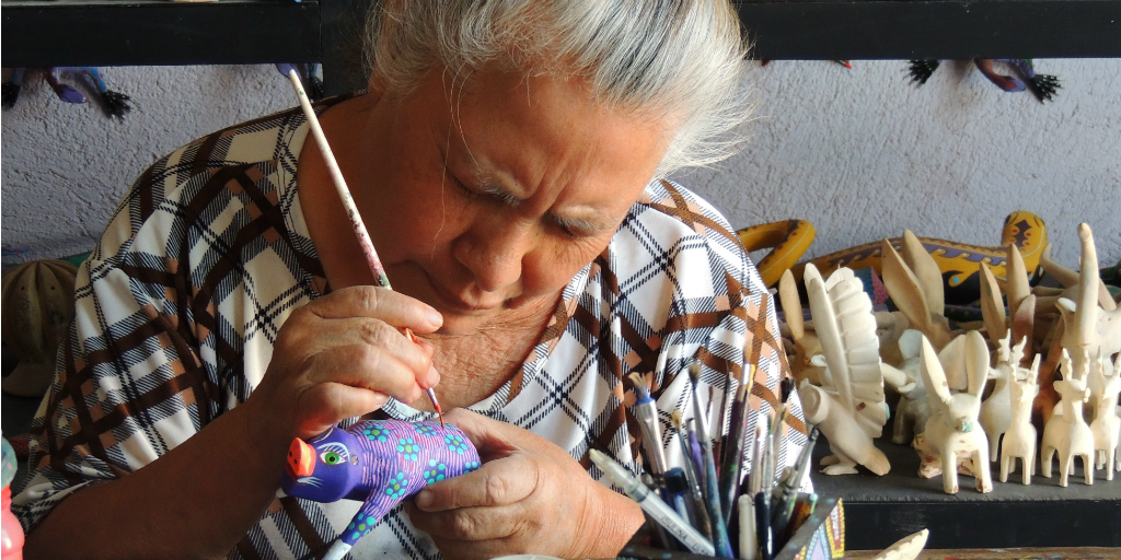An elderley Mexican woman hand-painting a ceramic animal.