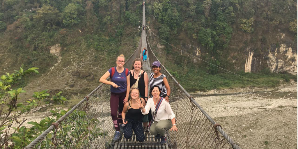 A group of hikers pose for a photo on a suspension bridge.