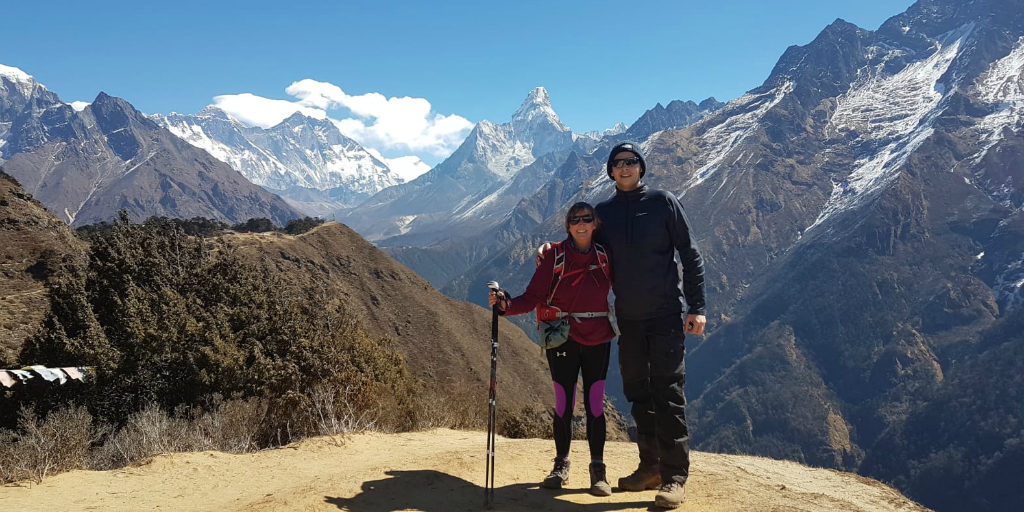 Two hikers pose for a photo with a mountain peak in the background.
