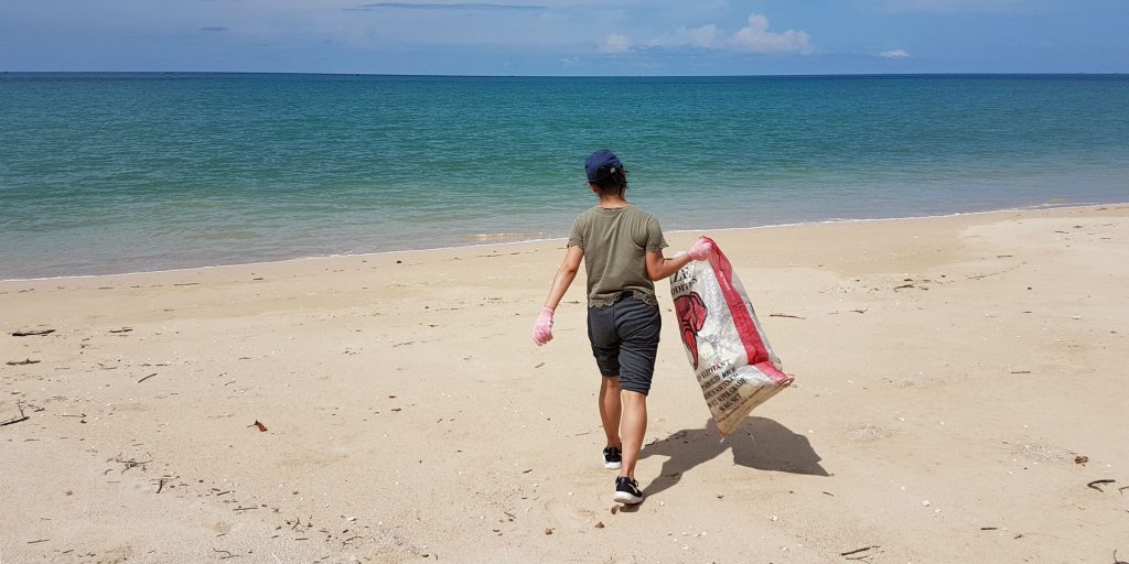 A volunteer carrying a large hessian bag across the beach.