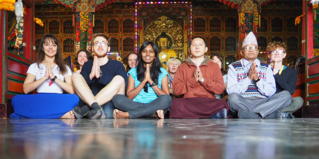 Volunteers sitting on the floor of a temple with a Nepalese man.