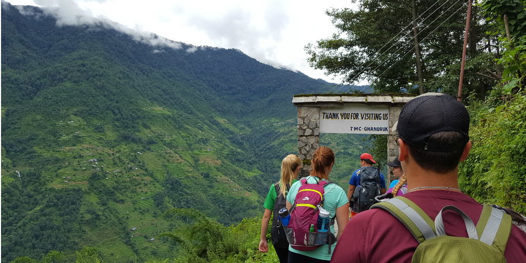 Hikers walking through an arch on a hiking trail in single file.