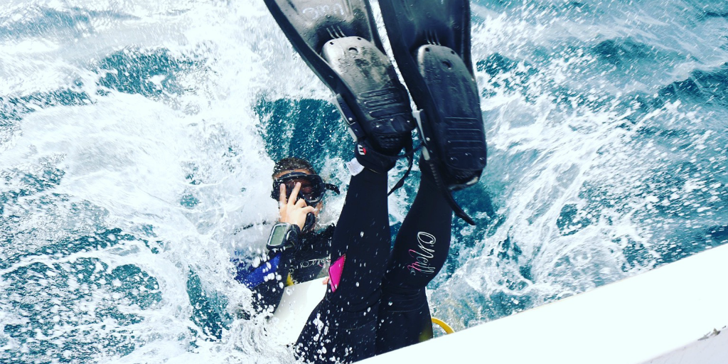 A diver back-rolling off of the side of a boat and into the ocean.