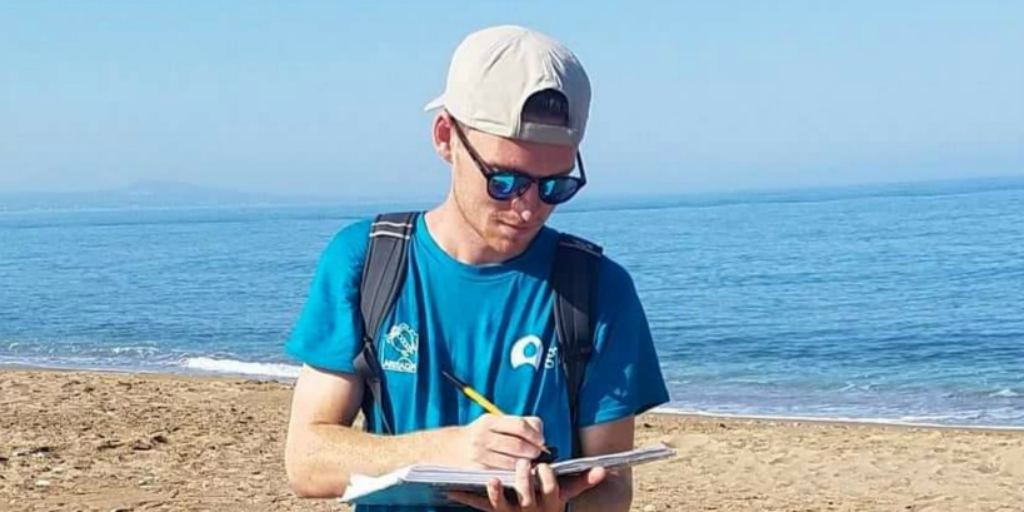 A volunteer writing on a clipboard with the ocean in the background.