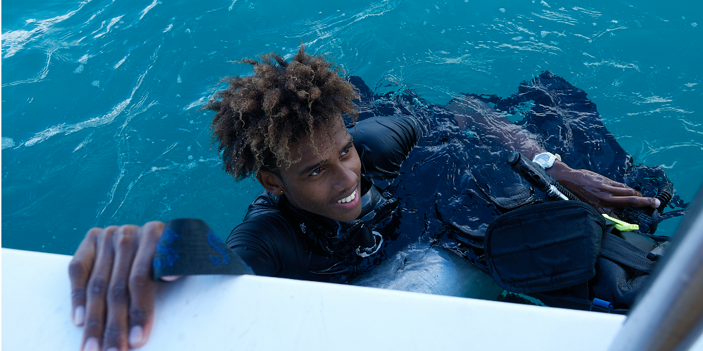 A diver holding onto the edge of a boat as he floats with his head above the surface.