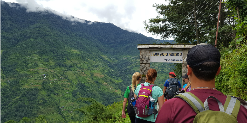 A row of hikers walking towards an arch on a mountain pathway in Pokhara.