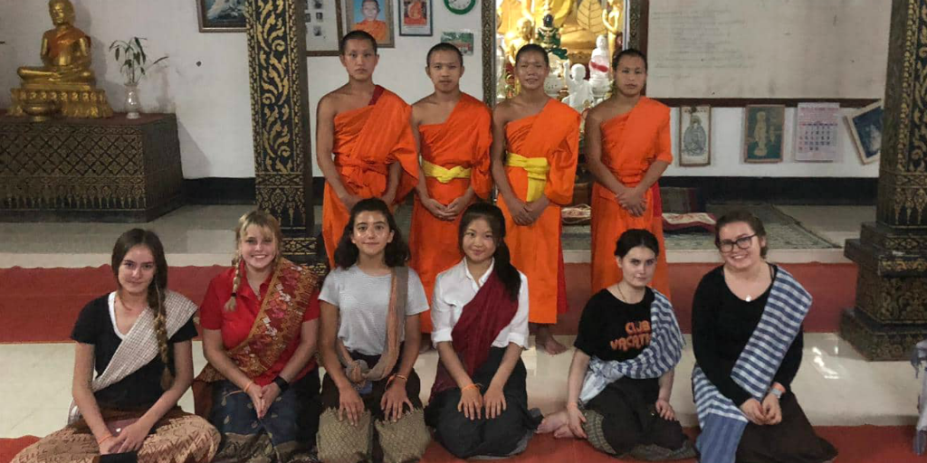 Volunteers kneeling in front of novice Buddhist monks in temple in Thailand.