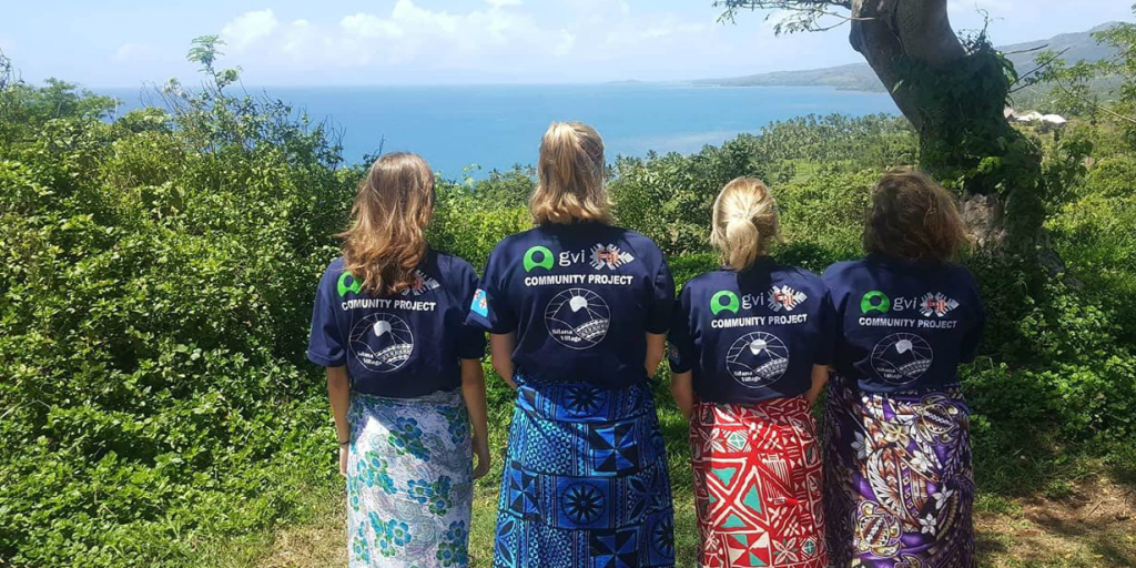 Four volunteers standing in a line and looking out over the ocean.