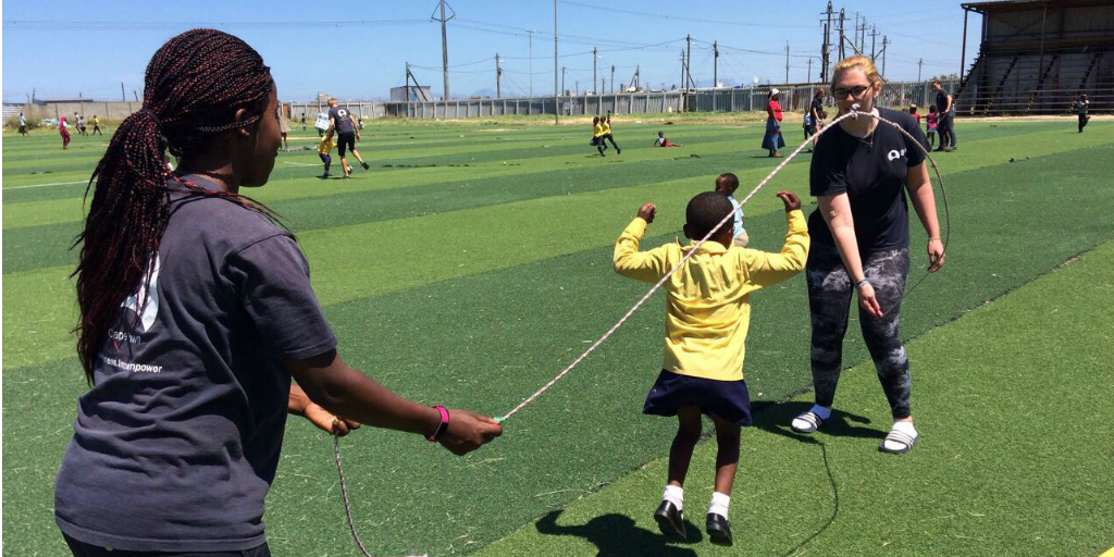 Volunteers swinging a skipping rope while a child jumps over the rope.