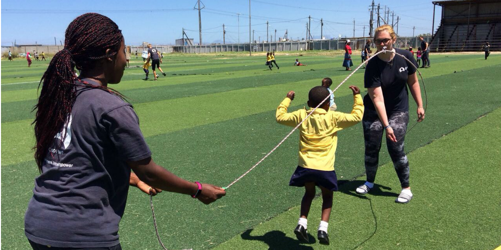 Volunteers swinging a skipping rope while a child jumps over the rope.