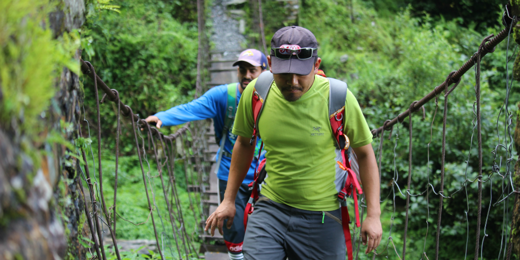 Two men walking across a suspension bridge in the jungle.