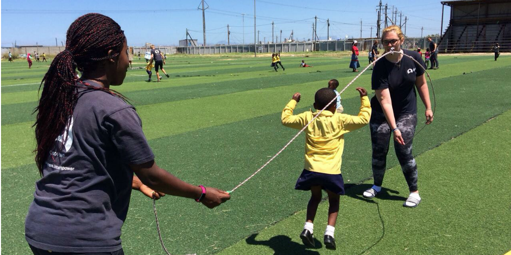 Volunteers swinging a skipping rope on a sports field while a child jumps the rope.