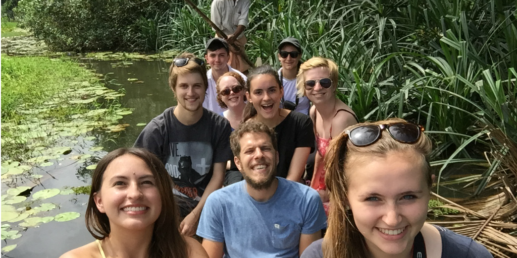 A group of volunteers in a boat being steered by a guide with an oar.