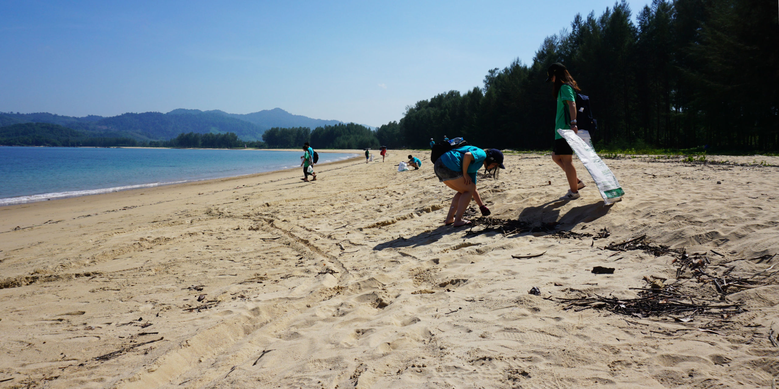 A pair of participants collect litter from a beach while taking a gap year in Thailand.