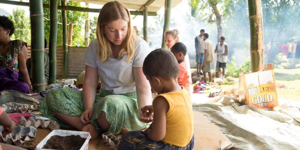 A GVI volunteer helps a child plant a seed for a gardening project. 