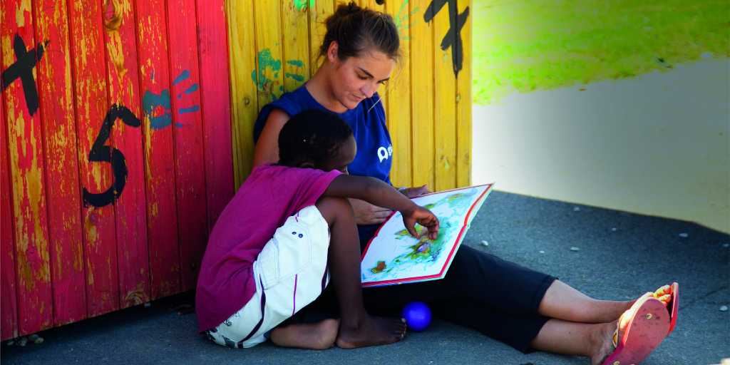 A GVI volunteers helps a child read a book. 